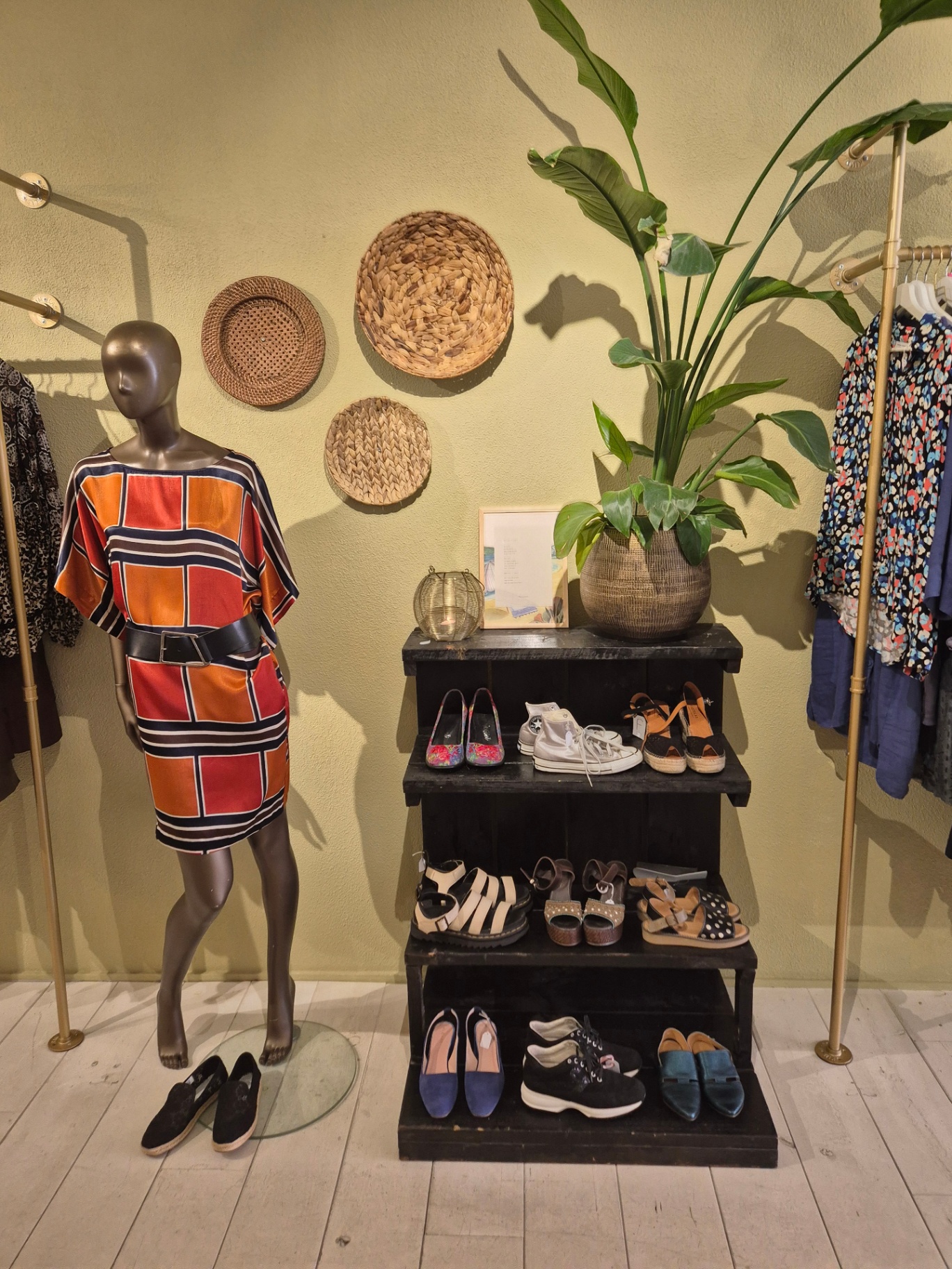 Etalagepop in kleurrijke jurk naast een display met schoenen en rieten manden.