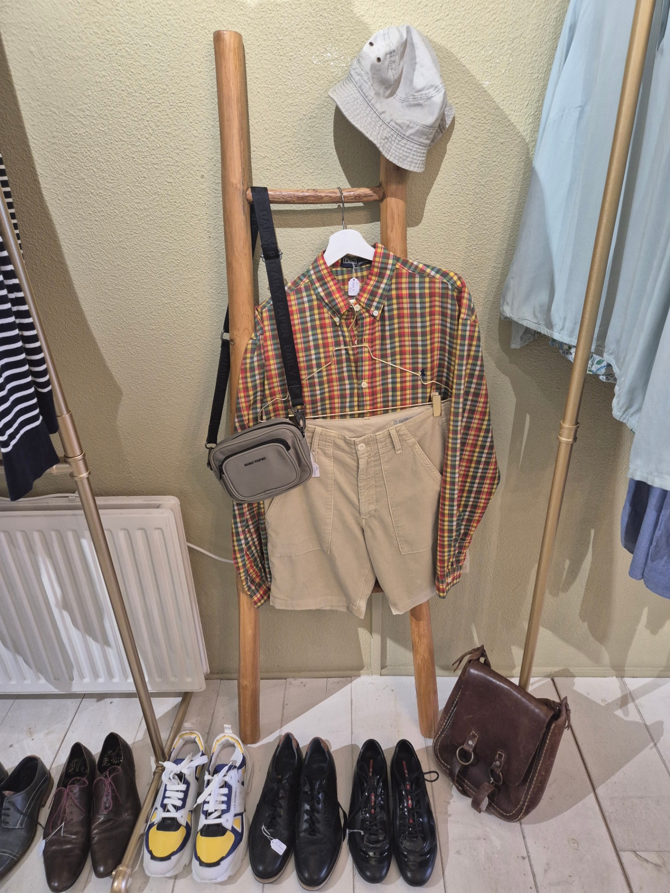 Houten ladder met geruit overhemd, corduroy short, hoedje en schoudertas · styling in de winkel.