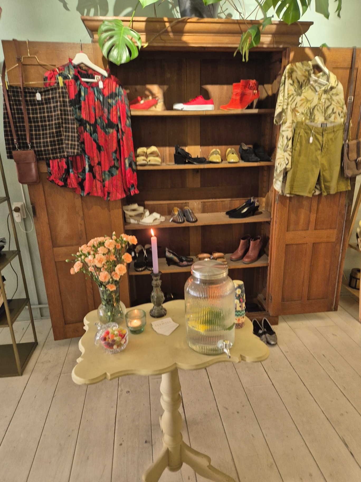 Bijzettafeltje met bloemen, kaars en waterkaraf voor een antieke kast met schoenen en kleding.