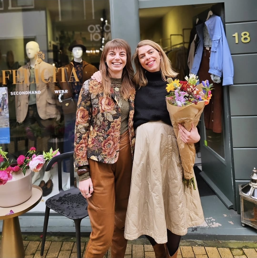 Femke en Esther samen voor de winkelpui van Felicità aan de Zwanestraat 18 in Groningen, met een boeket bloemen.
